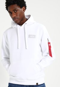 Witte hoodie met een ritszak op de mouw, voorzien van een logo patch en een koordcapuchon. Getextureerde stof, eenvoudig ontwerp en een losse pasvorm.