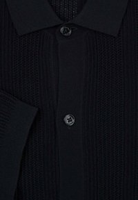 Cardigan nero a maglia con colletto classico, motivo texturizzato e chiusura a quattro bottoni. Sono visibili dettagli a coste sulle maniche e sul corpo.