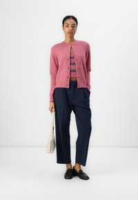 Rózsaszín, texturált kardigán gombokkal, csíkos crop top fölött viselve, navy színű, bő szárú nadrággal és fekete slip-on cipőkkel párosítva.