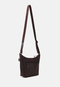 Sac à dos en cuir marron avec une longue bandoulière réglable, une poche frontale zippée et une texture lisse. Design arrondi en haut pour un accès facile.