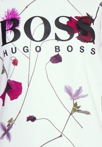 Textil blanco con texto grande en negro "BOSS" y logotipo "HUGO BOSS". Estampado floral en morado, rojo y enredaderas verdes con diversas flores.