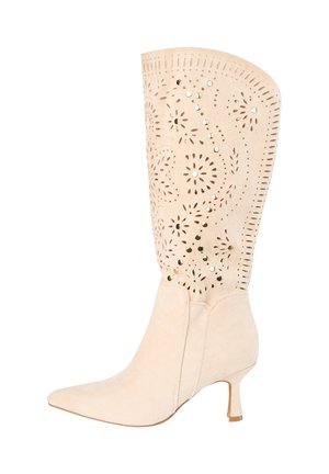 Beige kniehoog suède laarsje met puntige neus, smalle hak en ingewikkelde uitgesneden bloem- en geometrische patronen op de schacht.