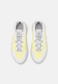 Vita sportskor med gula accenter, med en slät yta, rund form och tunna snören. Logotyp synlig på plösen.