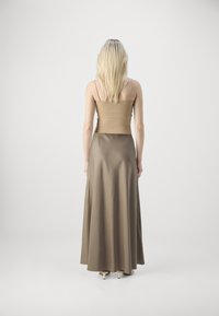 Pitkä, ruskea mekko, jossa on tiukka yläosa ja virtaava hame. Valmistettu sileästä materiaalista, jossa on ohuet hihnat ja hienovarainen kiilto.