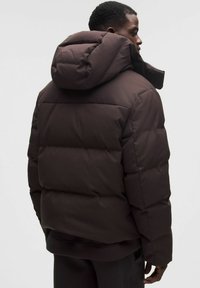 Ruskea puhujatakki, jossa on huppu, tikattu muotoilu ja lyhyt pituus. Silkkinen, eristetty kangas, jossa on näkyvät ompelu yksityiskohdat.