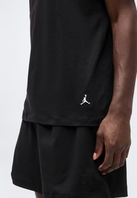 Σετ μαύρα σορτς και μπλουζάκι που φοριέται από ένα άτομο, με λευκό λογότυπο Jumpman στο μπλουζάκι και μαύρο σήμα Nike στα σορτς.