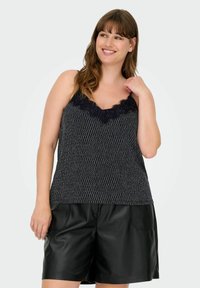 Camiseta de tirantes con estampado en blanco y negro y encaje en el escote, combinada con pantalones cortos de cuero negros. Textura suave con tirantes ajustables.