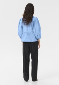 Top azzurro chiaro con maniche a sbuffo, vita a peplo e orlo scallop, abbinato a pantaloni larghi a righe nere. Tessuto morbido, vestibilità comoda.