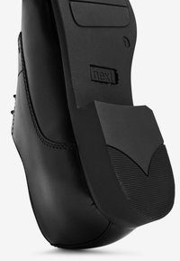 Černá formální podrážka s vyraženým logem "next", ukazující detailní švy a texturovaný podpatek na bílém pozadí.