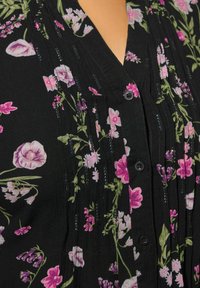 Blusa nera con stampa floreale multicolore nei toni del rosa e del verde. Dettagliata con bottoni e pieghe verticali. Tessuto morbido e testurizzato.