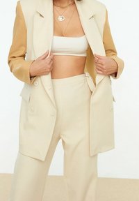 Beige und sandfarbene zweifarbige Blazer mit taillierter Passform, weichem Material, großen Knöpfen und zwei vorderen Taschen, kombiniert mit passenden Hosen.