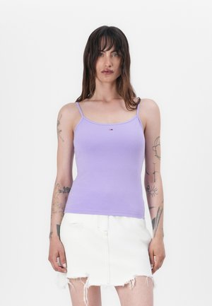 Lilac cotton tank top with thin straps, featuring a small logo on the chest. Paired with a white denim mini skirt with frayed hem.
