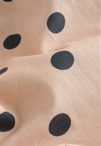 Tela de color rosa claro con grandes lunares negros, que muestra una textura tejida. El patrón está distribuido de manera uniforme por toda la superficie.