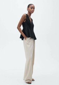Black sleeveless peplum top paired with light beige wide-leg trousers. Top features a V-neckline; smooth texture, simple design.
