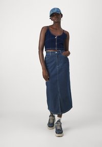 Modra skrajšana majica brez rokavov z zadrgo spredaj, kombinirana z jeans maksi krilom z sprednjim razporkom. Poudarjena z modrimi supergami in usklajeno kapo.