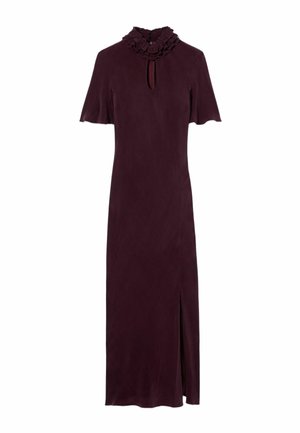 Femme portant une robe violet foncé à manches courtes, col à volants, encolure en forme de goutte, ceinture marron et sandales dorées à brides, debout devant un fond uni.