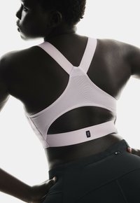Jasnoróżowy stanik sportowy z plecami w stylu racerback, z teksturowanym materiałem, wycięciami oraz logo na dolnej części pleców.