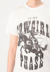 Witte katoen t-shirt met een zwarte grafische print van een cowgirl te paard, met de tekst "IN MY COWGIRL PHASE" prominent weergegeven.