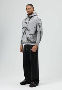 Grijze hoodie met zwart tie-dye patroon, voorkantzak, gecombineerd met zwarte, wijd uitlopende broek en chunky zwarte schoenen met roze accenten.