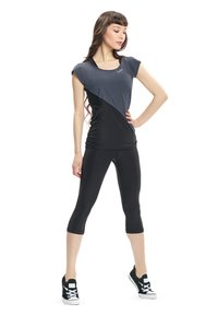 Top sportivo nera e grigia con maniche corte, abbinato a leggings capri neri. Modella che indossa scarpe da ginnastica nere; tessuto liscio, design aderente.