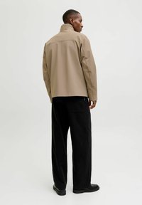 Bežna vodoodporna jakna z visokim ovratnikom, sproščenim krojem in izpostavljenim šivanjem. Kombinirana z širokimi črnimi hlačami in črnimi čevlji.