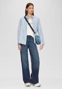 Lichtblau gestreepte overhemd met knopen boven een witte graphic t-shirt, gecombineerd met hoge taille donkerblauwe wijde jeans en sneakers.