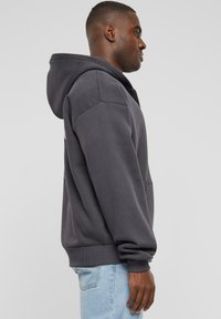 Gray hoodie with a kangaroo pocket, relaxed fit, ribbed cuffs and hem, made of soft cotton material, worn over light blue jeans.
