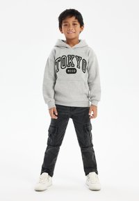 Sudadera gris con el texto "TOKYO" y "MOOD" debajo, combinada con pantalones cargo negros con bolsillos laterales y zapatillas blancas. Diseño sencillo, estilo casual.