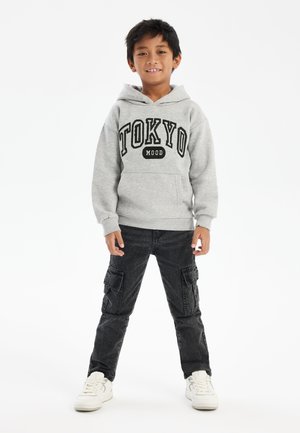 Sudadera gris con el texto "TOKYO" y "MOOD" debajo, combinada con pantalones cargo negros con bolsillos laterales y zapatillas blancas. Diseño sencillo, estilo casual.