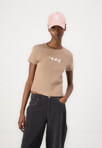 Brown cotton t-shirt with short sleeves and graphic designs, paired with dark gray pants. Pink cap with a white logo accent.