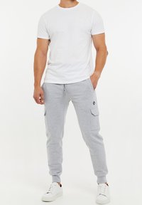 Vit bomullst-shirt kombinerad med grå mjukisbyxor med sidofickor och elastiska muddar, kompletterade med vita sneakers.