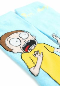 Calzini turchesi con un design ricamato di un personaggio sorpreso con occhi sbarrati e una maglietta gialla, esposti da un'angolazione.