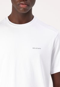 Fehér pamut póló kerek nyakkal és rövid ujjal, melyen egy kis szürke "BELSTAFF" logó látható a bal mellrészen. Simább tapintású.