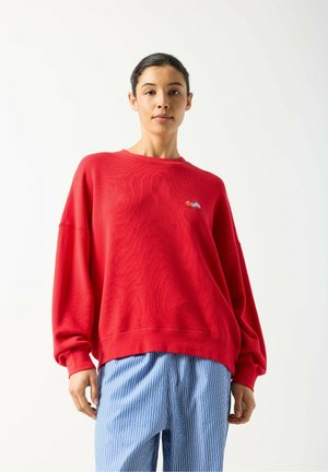 Felpa rossa con vestibilità comoda, polsini a coste e scollo rotondo. Presenta un piccolo ricamo sul petto. Abbinata a pantaloni a righe.