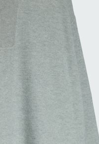 Tissu tricoté gris clair avec un patch rectangulaire côtelé sur un vêtement, montrant de près la texture et les coutures.