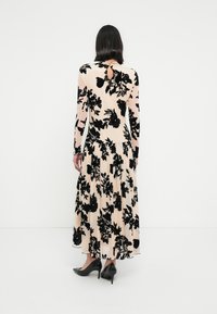 Φόρεμα με μακριά μανίκια και μαύρο λουλουδάτο σχέδιο σε ανοιχτόχρωμο φόντο, με άνοιγμα στην πλάτη, φούστα με βολάν και μαύρες ψηλοτάκουνες γόβες.