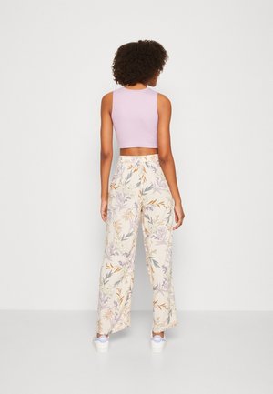 Lys lilla croptop kombineret med cremegule bukser med vide ben, dekoreret med et blomstermønster i lilla, grøn og orange og med snøre i taljen.