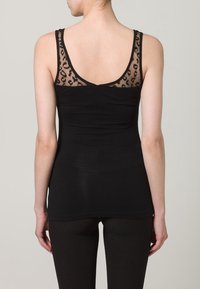 Svart linne med en genomskinlig leopardmönstrad panel på baksidan. Tyget är slätt med en åtsittande design och breda axelremmar.