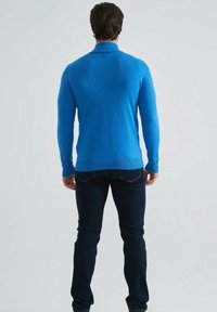 Pull en tricot bleu à coupe ajustée, avec des manches longues et un col rond, associé à un jean noir à coupe slim.
