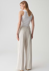 Top a canottiera bianca a costine abbinata a pantaloni larghi di un beige chiaro con una texture liscia e una vita elasticizzata.
