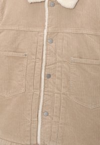 Beige kordflorsjacka med en foder av sherpa vid kragen, med två framfickor, silverfärgade metallknappar och vertikal ribbad textur.