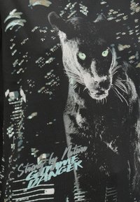 Čierna látka má grafiku pantera so zelenými očami. Dizajn je sprevádzaný textom svetlomodrej farby a obsahuje ozdoby.