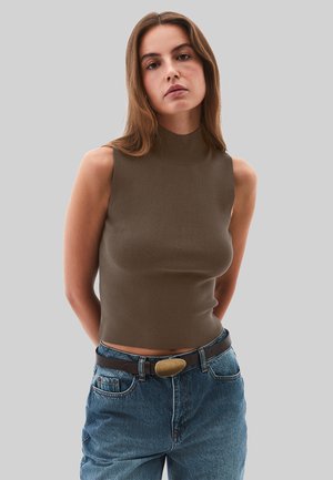 Bruine mouwloze coltrui van geribbelde stof, gecombineerd met high-waisted blauwe denim jeans en een bruine riem met een ronde gesp.