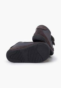 Scarpe in suede marrone con suola in gomma, dotate di una cintura a strappo e una superficie testurizzata. Il design è basso per una facile indossabilità e comfort.