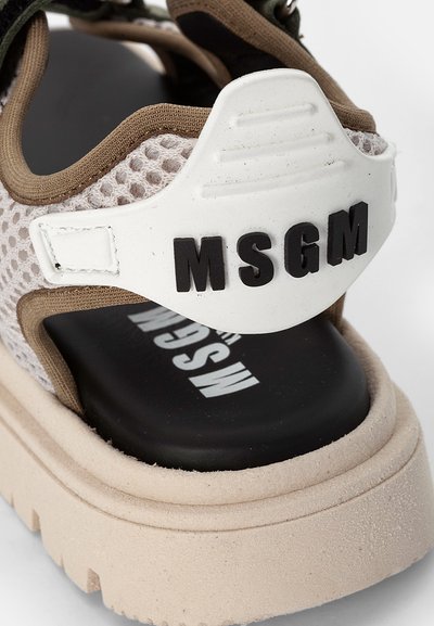 Sapatilha em malha com parte superior bege, tira de calcanhar em borracha branca com "MSGM" em preto, e sola robusta de cor clara.