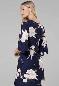Navy floral dress with bell sleeves, featuring white and peach flowers, smooth fabric, and a fitted silhouette. Back view showing floral design details.