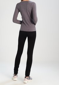 Gray ribbed long-sleeve top paired with black skinny jeans and gray sneakers. The outfit features fitted shapes and a casual design.