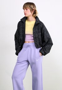 Juodas bomber tipo Justas su gėlėtomis spaudomis, trumpa forma, derinamas su geltonu ir pastelinės purpurinės spalvos prigludusiu palaidiniu bei alyvų spalvos sportinėmis kelnėmis su Nike logotipu.