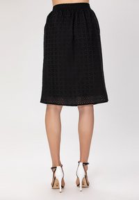 Jupe midi noire avec taille élastique, présentant un motif texturé. Associée à des chaussures à talons blancs avec des brides noires.