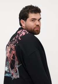 Black sweatshirt featuring a large pink floral design and intricate graphic on the back, with a relaxed fit and soft texture.